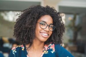 Smiling young woman with curly hair and glasses showcasing braces, emphasizing orthodontic care at Comfort Dental Braces in Federal Way, WA.