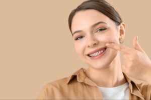 Smiling young woman with braces pointing to her teeth, representing orthodontic care by Comfort Dental Braces in Federal Way, WA.